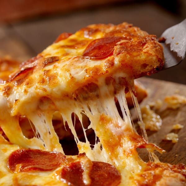 A slice of Positano's pepperoni pizza being lifted, with melted cheese stretching.