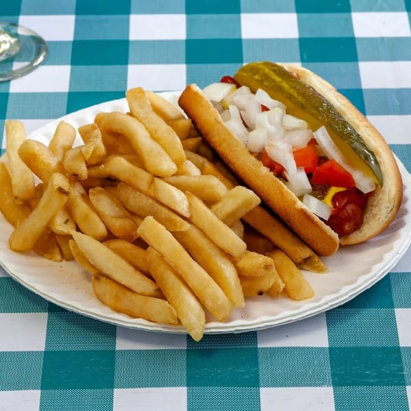 A hot dog with diced onions, tomatoes, mustard, ketchup, and a pickle spear, served with fries.