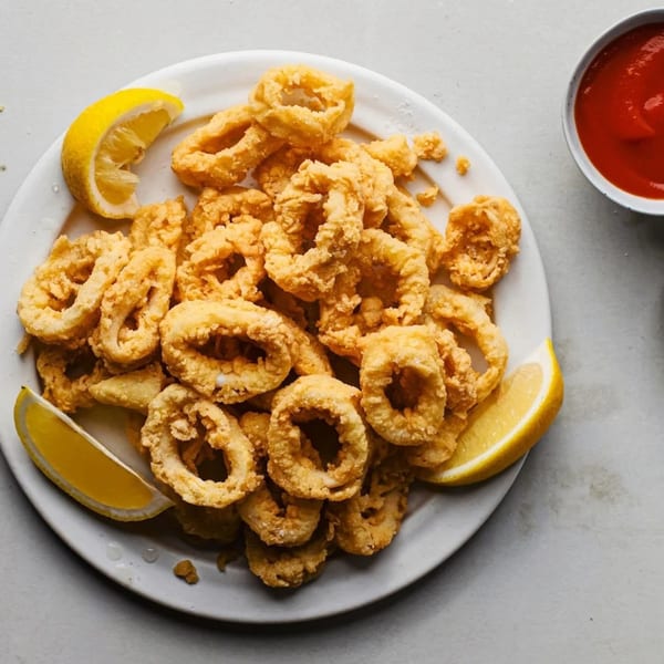 Crispy fried calamari rings with lemon wedges and a side of red sauce.