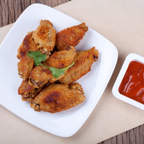 Crispy fried chicken wings with cilantro garnish on a white plate, served with a side of red sauce.