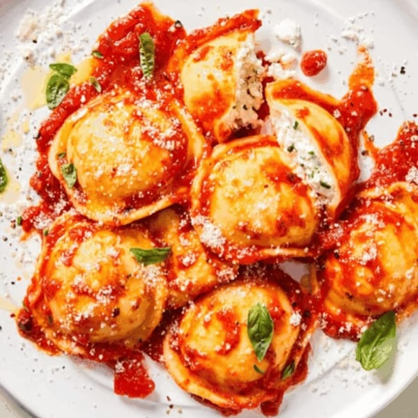 Plate of ravioli with red sauce, parmesan cheese, and basil, one ravioli split open.